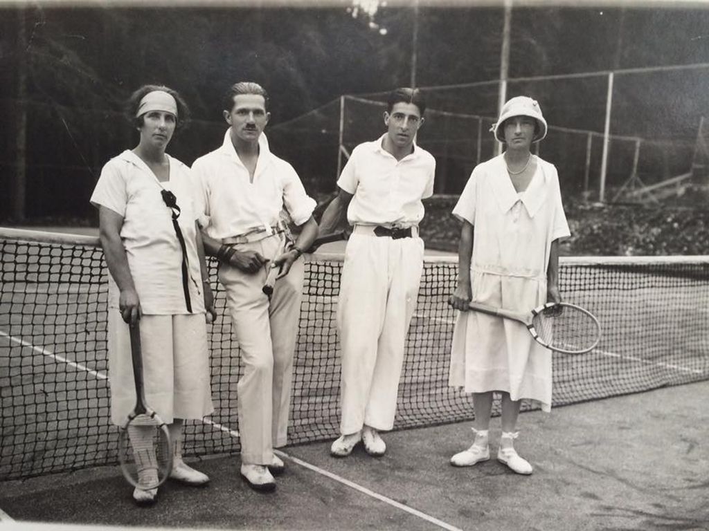 Une partie de tennis en double, avec des paires tout de blanc vêtues. 