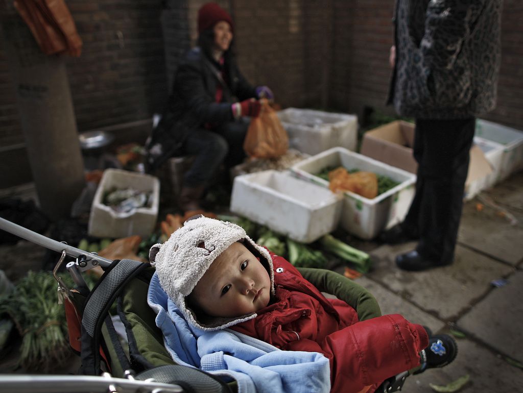 A baby sits in a carriage while a woman bought vegetables at a stall near a residential building in Beijing Monday, Feb. 28, 2011. China is slightly lowering its annual economic growth target, to 7 percent from 8 percent, the premier said Sunday, in a move that signals a shift in government priorities to put the breakneck economy on a more sustainable footing. (AP Photo/Andy Wong)