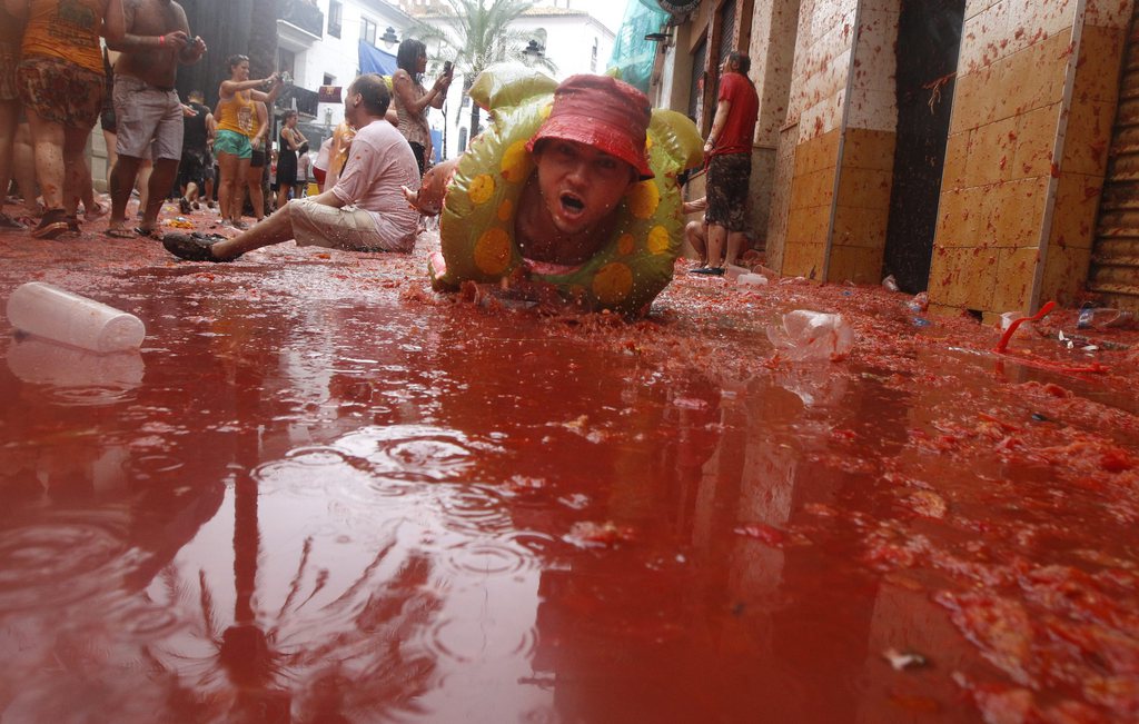 A man lays on a puddle of tomato juice during the annual "tomatina" tomato fight fiesta in the village of Bunol, 50 kilometers outside Valencia, Spain, Wednesday, Aug. 28, 2013. Thousands of people are splattering each other with tons of tomatoes in the annual "Tomatina" battle in recession-hit Spain, with the debt-burdened town charging participants entry fees this year for the first time. Bunol town says some 20,000 people are taking part in Wednesday's hour-long street bash, inspired by a food fight among kids back in 1945. Participants were this year charged some 10 euros ($13) to foot the cost of the festival. Residents do not pay. (AP Photo/Alberto Saiz)