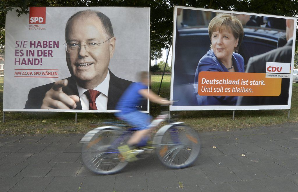 A man on a bicycle passes election posters, showing the two top candidates for next German chancellor at a street in Duisburg, western Germany, Thursday, Aug. 29, 2013. Peer Steinbrueck of the Social Democratic Party, SPD, left, will challenge German chancellor Angela Merkel of the governing Christian Social Democrats, CDU, right. Germans will vote on Sept. 22, 2013. Slogan on the SPD poster reads "you have it in your hand" and on the CDU poster "Germany is strong. And should stay that way." (AP Photo/Martin Meissner)
