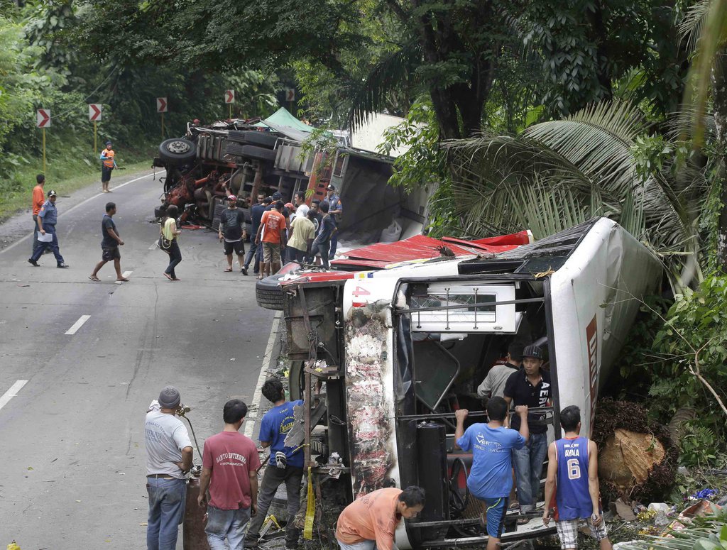 Workers sift through the wreckage of a passenger bus after getting involved in a seven-vehicle pile up along the highway at Atimonan township, Quezon province, about 115 kilometers (72 miles) southeast of Manila, Philippines Saturday Oct. 19, 2013.  A truck, seen in the background, carrying hog feed smashed into the rear of a passenger bus on a remote downhill provincial road in the Philippines early Saturday, setting off a series of wrecks that left at least 20 people dead and injured 44 others, police said. The bus driver lost control of his vehicle after the first collision and hit two buses and four vans coming from the opposite direction before toppling over on the narrow downhill road in Quezon province, police chief Jonar Yupio said. (AP Photo/Bullit Marquez)