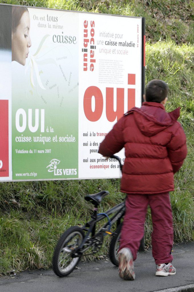 Un enfant passe devant des affiches sur les prochaines votations federales concernant la caisse unique, ce mercredi 7 mars 2007 a Geneve. Les citoyens suisses voteront sur l'initiative "pour une caisse maladie unique et sociale" lors de la votation federale du 11 mars 2007. (KEYSTONE/Salvatore Di Nolfi)