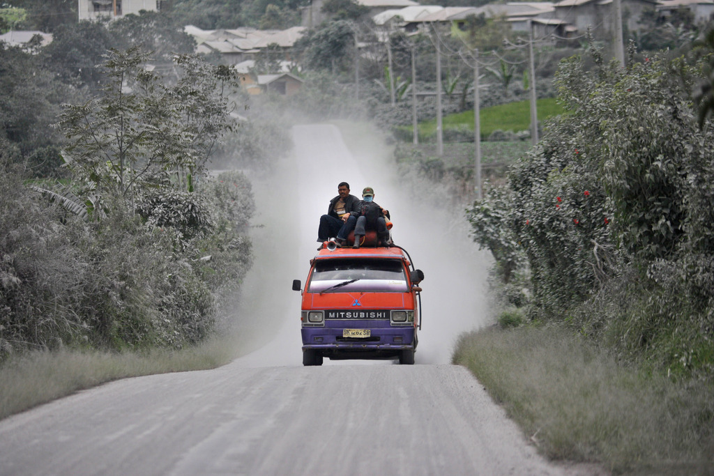 Villagers ride on top of a van on a road covered with volcanic ash from the eruption of Mount Sinabung in Sigarang Garang, North Sumatra, Indonesia, Monday, Nov. 25, 2013. Powerful bursts of hot ash and gravel erupted from the rumbling volcano in western Indonesia Monday, a day after authorities had raised the volcano's alert status to the highest level. (AP Photo/Binsar Bakkara)