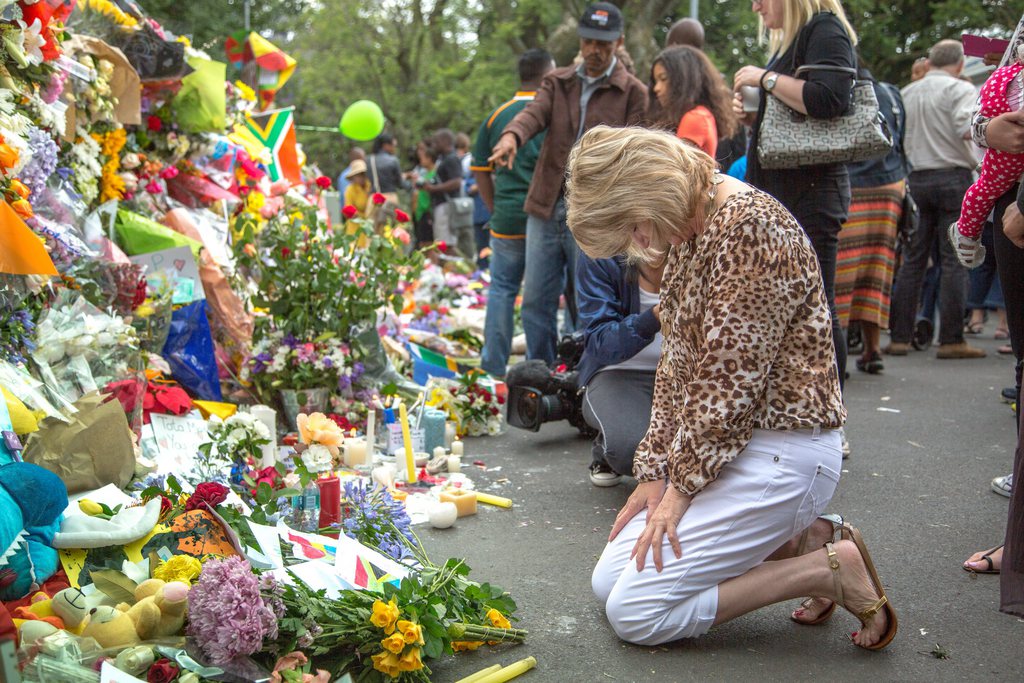 epa03980791 A woman bows in front of a wall of flowers as people pay tribute to former South African president and Nobel Peace prize laureate Nelson Mandela outside his Houghton home where he died in Johannesburg, South Africa, 07 December 2013. Nobel Peace Prize winner Nelson Mandela died at age 95, in Johannesburg, South Africa, on 05 December 2013. A former lawyer, Mandela was the first black President of South Africa voted into power after the countries first free and fair democratic elections that witnessed the end of the Apartheid system in 1994. Mandela was founding member of the ANC (African National Congress) and anti-apartheid activist who served 27 years in prison, spending many of these years on Robben Island. In South Africa, Mandela is often known as Tata Madiba, an honorary title adopted by elders of Mandela's clan. Mandela won the Nobel Peace Prize in 1993.  EPA/TJ LEMON