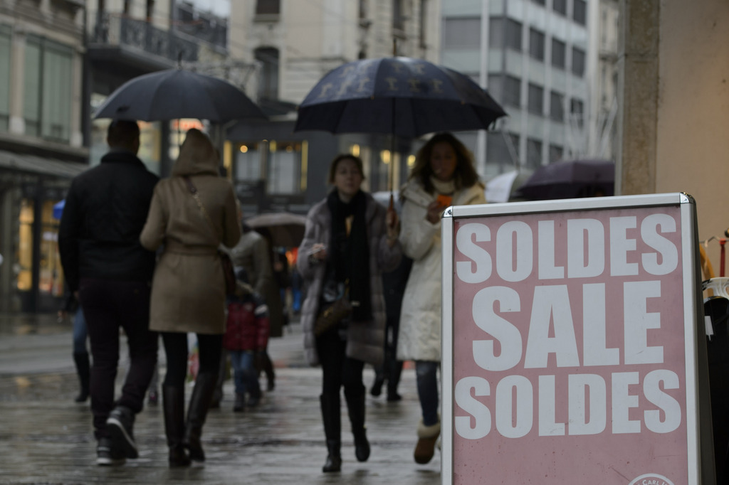 Des personnes passent devant un panneau d'un magasin annoncant les soldes, dans les rues du centre ville de Geneve, ce samedi 4 janvier 2014. (KEYSTONE/Martial Trezzini)