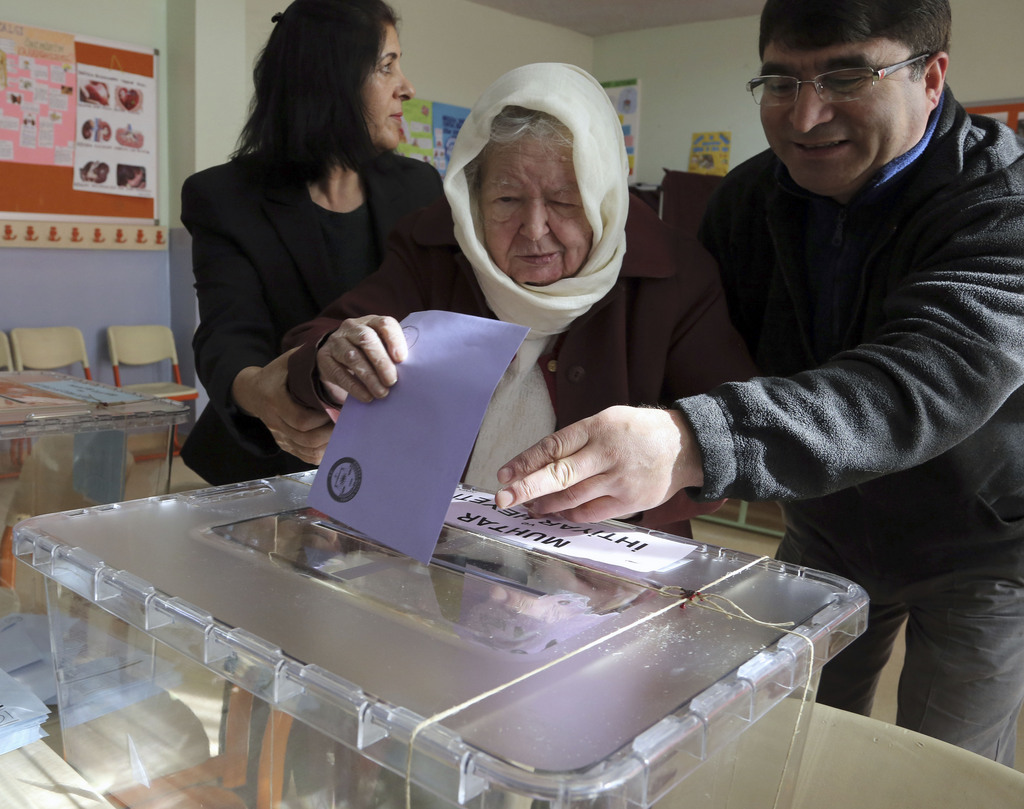 Melek Betul Sinoplu, a Turkish woman, 87, is helped by officials to cast her ballot at a polling station in Ankara Turkey, Sunday, March 30, 2014. More than 52 millions Turks vote in local elections Sunday as Turkish Prime Minister Recep Tayyip Erdogan is fighting corruption allegations against his government. The local elections are seen as a referendum over his rule. (AP Photo/Burhan Ozbilici)