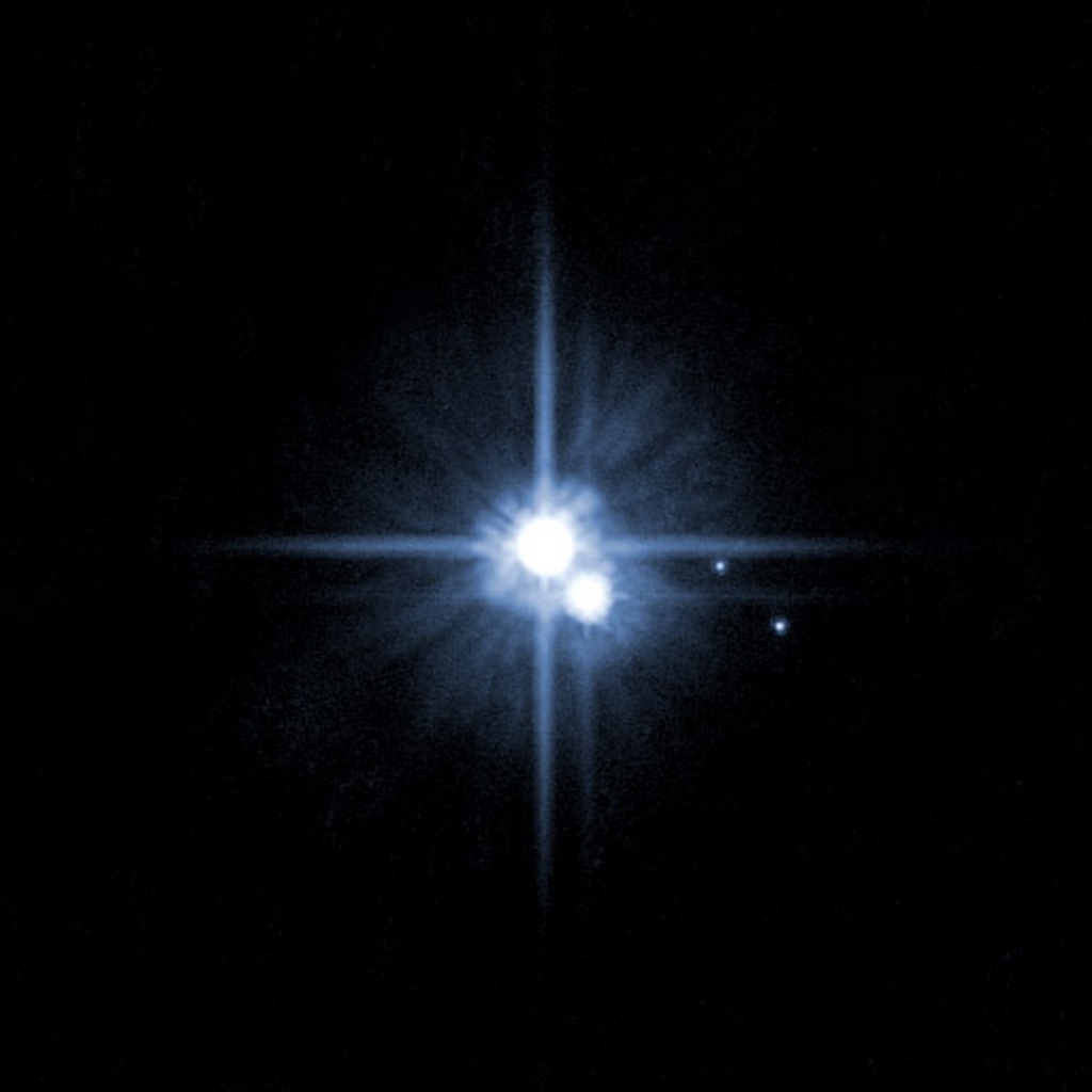 Pluton, dépossédé de son statut de planète en 2006 serait en passe de le récupérer. Ici, on distingue l'astre, entouré de trois de ses cinq lunes.