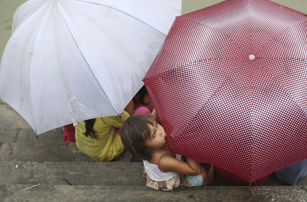A Filipino girl bites an umbrella as her playmates take cover from rain in Makati, south of Manila, Philippines on Sunday, Sept. 14, 2014. The Philippine weather bureau says Typhoon Kalmaegi was located based on all available data at 266 km North Northeast of Virac, Catanduanes or at 347 km East Southeast of Casiguran, Aurora with maximum winds of 120 kph and gustiness of up to 150 kph. It is forecast to move West Northwest at 20 kph. (AP Photo/Aaron Favila)
