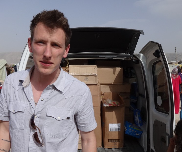 This undated photo provided by Kassig Family shows Peter Kassig standing in front of a truck filled with supplies for Syrian refugees. A video purportedly produced by militants in Syria released Friday, Oct. 3, 2014, shows Kassig, of Indianapolis, kneeling on the ground as a masked militant says he will be killed next. (AP Photo/Courtesy Kassig Family)