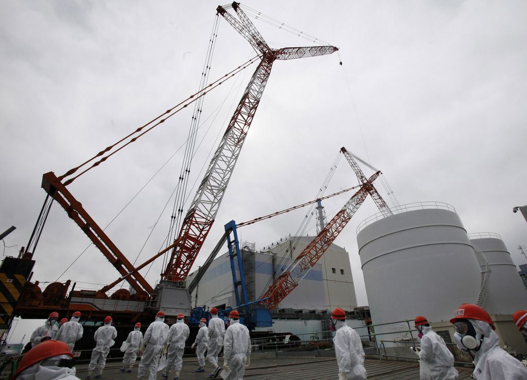 FILE - In this March 10, 2014 file photo, Tokyo Electric Power Co. (TEPCO) staff and journalists walk in front of the No. 1 reactor at the Fukushima Dai-ichi nuclear power plant during a press tour in Okuma town, Fukushima prefecture, northeastern Japan. A Japanese judicial panel has recommended that three former executives of the utility that operates the damaged Fukushima nuclear plant face criminal charges over their role in the disaster. A document released by the panel on Thursday, July 31, 2014 showed it voted in favor of indicting Tsunehisa Katsumata, chairman of Tokyo Electric Power Co. at the time of the crisis, along with two Vice Presidents Sakae Muto and Ichiro Takekuro.  The cleanup effort continues, and its decommissioning is expected to last decades. (AP Photo/Koji Sasahara, Pool, File)