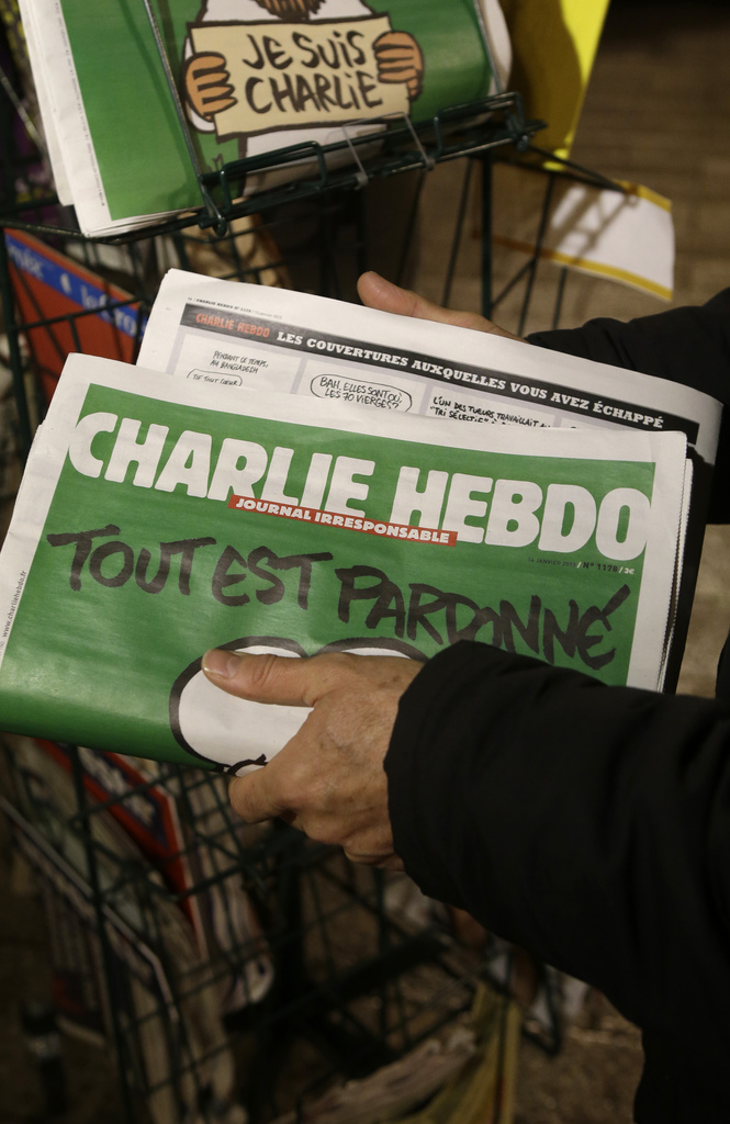 A seller of newspapers installs in shelf, several Charlie Hebdo newspapers at a newsstand in Nice southeastern France, Wednesday, Jan. 14, 2015. On front page reading "All is forgiven". Charlie Hebdo's defiant issue is in print, with a caricature of the Prophet Muhammad on the cover and a double-page spread claiming that more turned out Sunday to back the satirical weekly "than for Mass." Twelve people died when two masked gunmen assaulted the newspaper's offices on Jan. 7, including much of the editorial staff and two police. (AP Photo/ Lionel Cironneau)