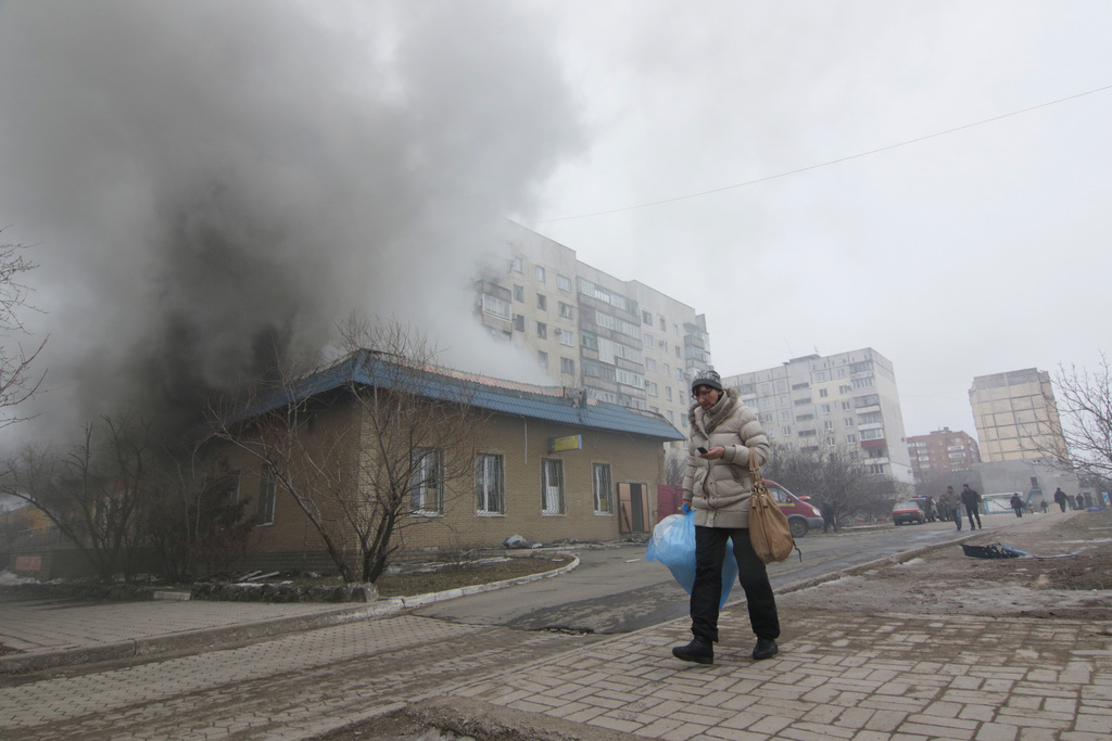 A woman resident passes by a burning house in Mariupol, Ukraine, Saturday, Jan. 24, 2015. A crowded open-air market in Ukraine's strategically important coastal city of Mariupol came under rocket fire Saturday morning, killing at least 10 people, regional police said. Heavy fighting in the region in the autumn raised fears that Russian-backed separatist forces would try to establish a land link between Russia and Crimea. Pro-Russian separatist forces have positions within 10 kilometers (six miles) from Mariupol's eastern outskirts. (AP Photo/Sergey Vaganov)
