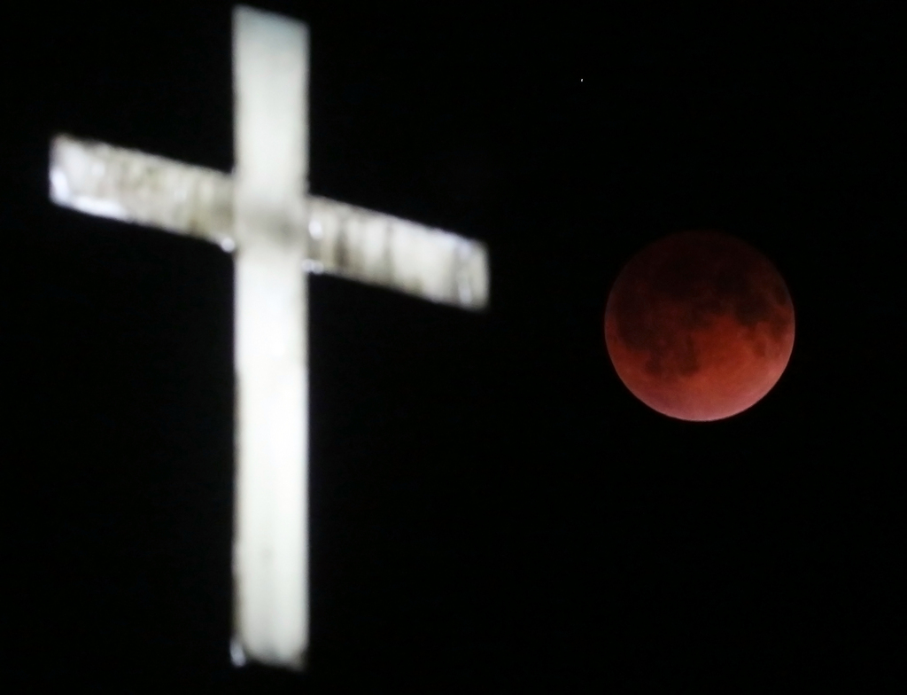 The Earth's shadow renders the moon in a crimson hue during a total lunar eclipse behind the illuminated steeple of St. Olaf Lutheran Church in the town of Ashippun , Wis. Tuesday, April 15, 2014. (AP Photo/Wisconsin State Journal, John Hart)