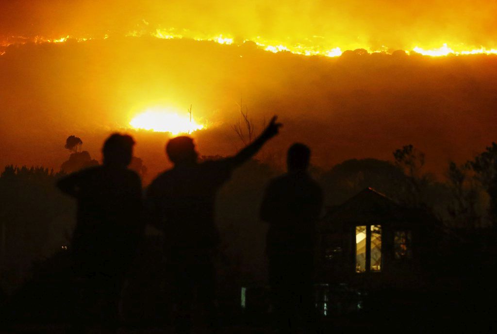epa04644019 Residents stand outside their homes as a fire aproaches in Noordhoek, Cape Town, South Africa, 02 March 2015. A fire fanned by gale force south easterly winds has raged across the south peninsula of Cape Town from Muizenberg to Hout Bay. Residents in some areas were forced to evacuate. Rescue personnel continue to battle the blaze.  EPA/NIC BOTHMA
