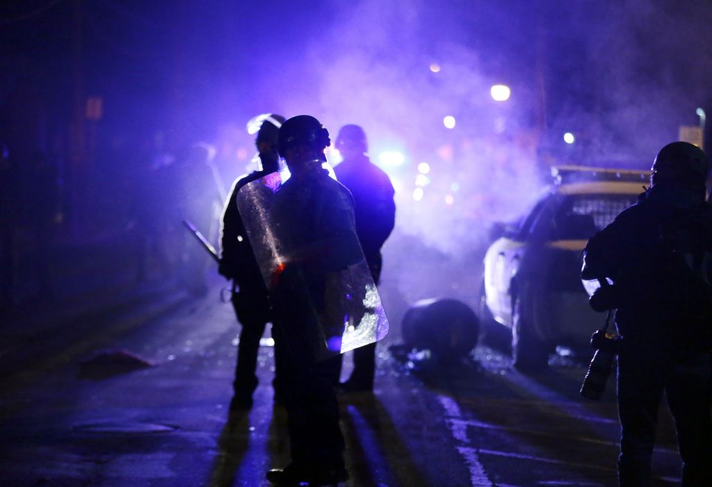 FILE - In this Nov. 25, 2014 file photo, police officers watch protesters as smoke fills the streets in Ferguson, Mo. after a grand jury's decision in the fatal shooting of Michael Brown. Newly released documents reveal that police planning for a grand jury announcement wanted Guard troops and armored Humvees stationed in the Ferguson neighborhood where Brown had been shot. But the records show the requests were not granted, because Missouri Gov. Jay Nixon preferred to use the Guard in a support role to police. (AP Photo/Charlie Riedel, File)