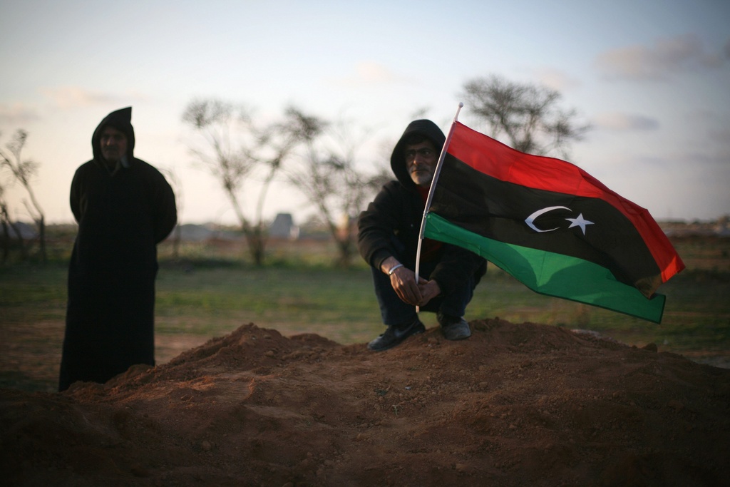 Libyan men, one waving a pre-Gadhafi flag, attend a funeral in Benghazi, Libya, Monday, March 5, 2012 for victims buried in a mass grave. Thousands of mourners gathered Monday in the eastern Libyan city of Benghazi to bury 155 bodies unearthed from a mass grave of people were killed during last year's civil war. It was the largest grave yet to be discovered from the conflict that began as a popular uprising and ended with the capture and killing of Libyan leader Moammar Gadhafi last October.(AP Photo/Manu Brabo)