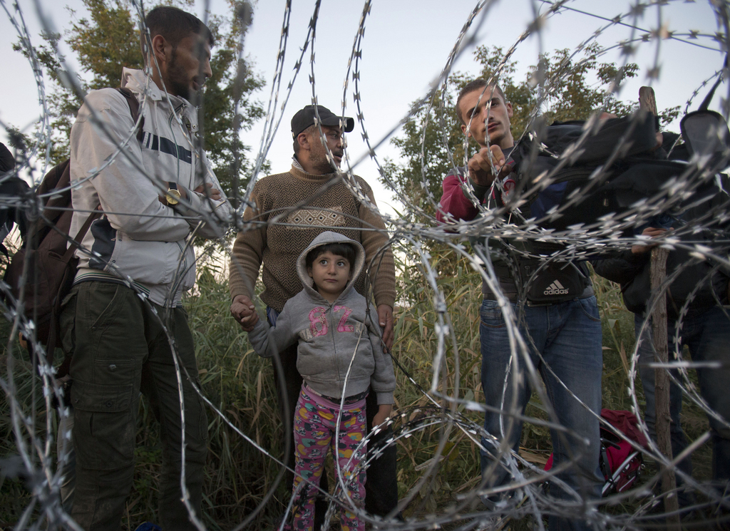 Syrian refugees wait at the barbed wire fence, on the border between Hungary from Serbia, near Roszke, Friday, Aug. 28, 2015. Hungary deployed police reinforcements to rein in an unrelenting flow of migrants across its porous border Thursday, but refugee activists said the effort appeared futile in a nation whose migrant camps are overloaded and barely delay their journeys west into the heart of the European Union. (AP Photo/Darko Bandic)