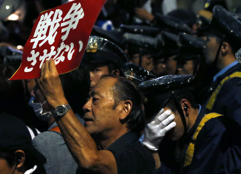 A protester shouts a slogan, beside a police officer during a rally against Japanese government in front of the parliament building in Tokyo, Friday, Sept. 18, 2015. Japan's parliament is moving toward final approval of legislation that would loosen post-World War II constraints placed on its military, an issue that has sparked sizeable street protests and raised fundamental questions about whether the nation needs to shift away from its pacifist ways to face growing security challenges. The placard reads: "No war." (AP Photo/Shuji Kajiyama)