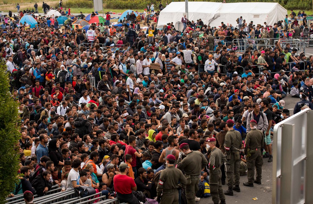 Migrants queue up for buses after they arrived at the border between Austria and Hungary near Heiligenkreuz, about 180 kms (110 miles) south of Vienna, Austria, Saturday, Sept. 19, 2015. Thousands of migrants who had been stuck for days in southeastern Europe started arriving in Austria early Saturday after Hungary escorted them to the border.  (AP Photo/Christian Bruna)