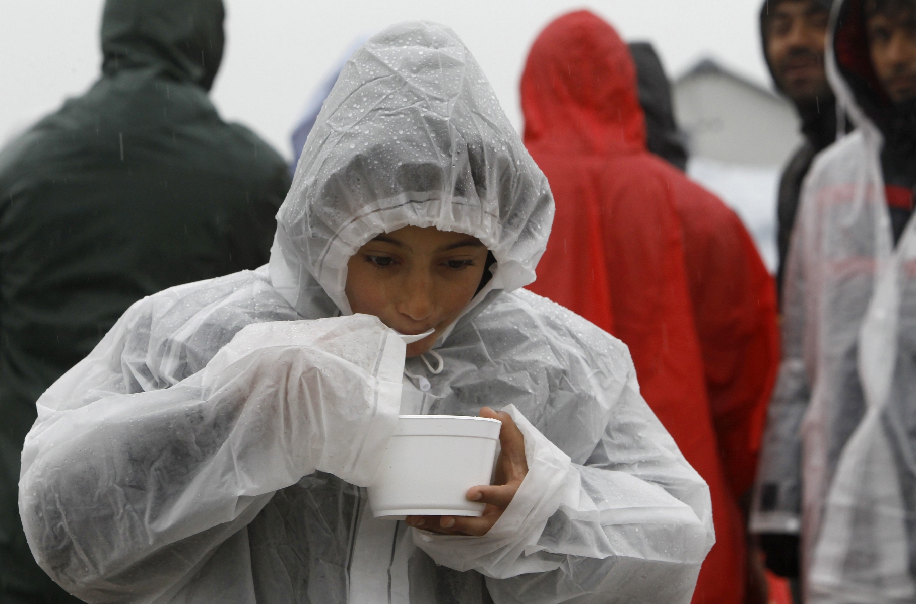 A refugee boy eats soup, provided by humanitarian workers, while walking in the rain through an improvised camp on the border line between Macedonia and Serbia near the northern Macedonian village of Tabanovce, Thursday, March 10, 2016. Around 1.500 migrants and refugees are stranded at Tabanovce transit center for refugees in northern Macedonia. (AP Photo/Boris Grdanoski) Macedonia Migrants