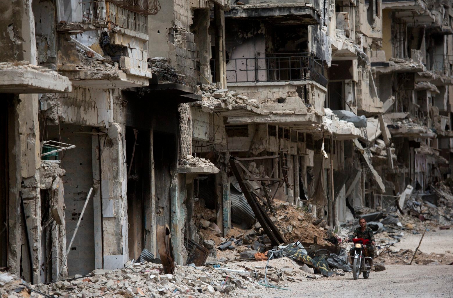 FILE - In this Thursday June 5, 2014 file photo, a man rides a motorcycle in a devastated part of Homs, Syria. (AP Photo/Dusan Vranic, File) Mideast Syria Timeline