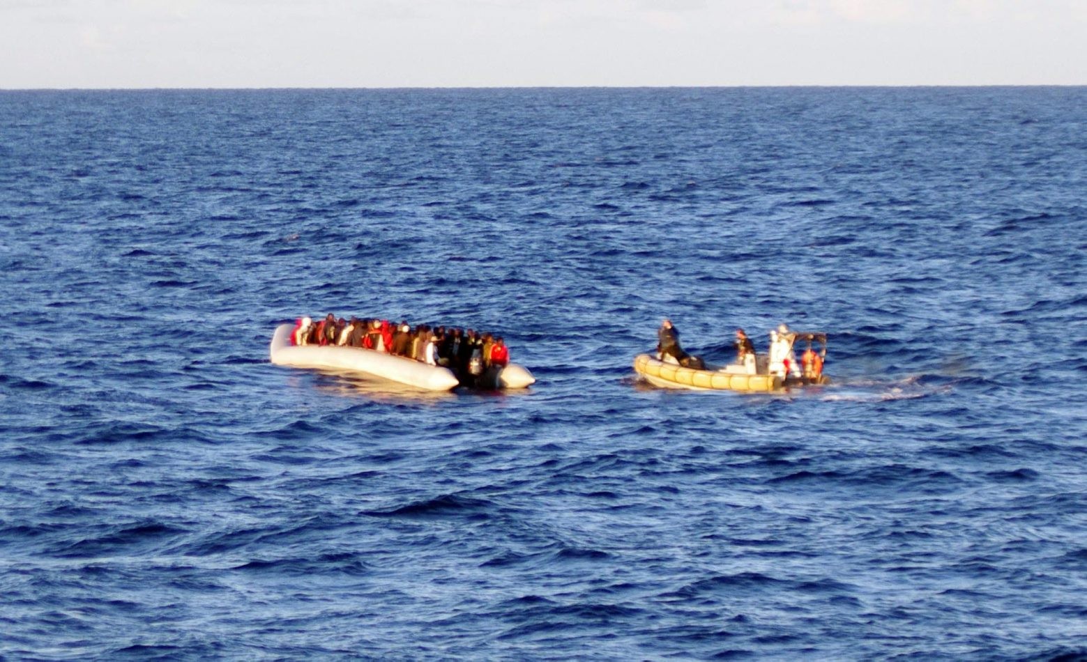 In this photo taken on Thursday, Dec. 4, 2014 provided by the Italian Navy, a rescue crew on a dinghy, right, approaches migrants on a boat some 40 miles (65 kilometers) from the Libyan capital, Tripoli. Rescue crews discovered 16 bodies in a migrant boat off Libya, the first reported deaths since the European Union took over Mediterranean rescue operations, the Italian navy said Friday. The EU operation, launched last month after Italy phased out its more robust rescue program, foresees patrols 30 miles (50 kilometers) from the Italian coast. (AP Photo/Italian Navy) Italy Migrants Deaths