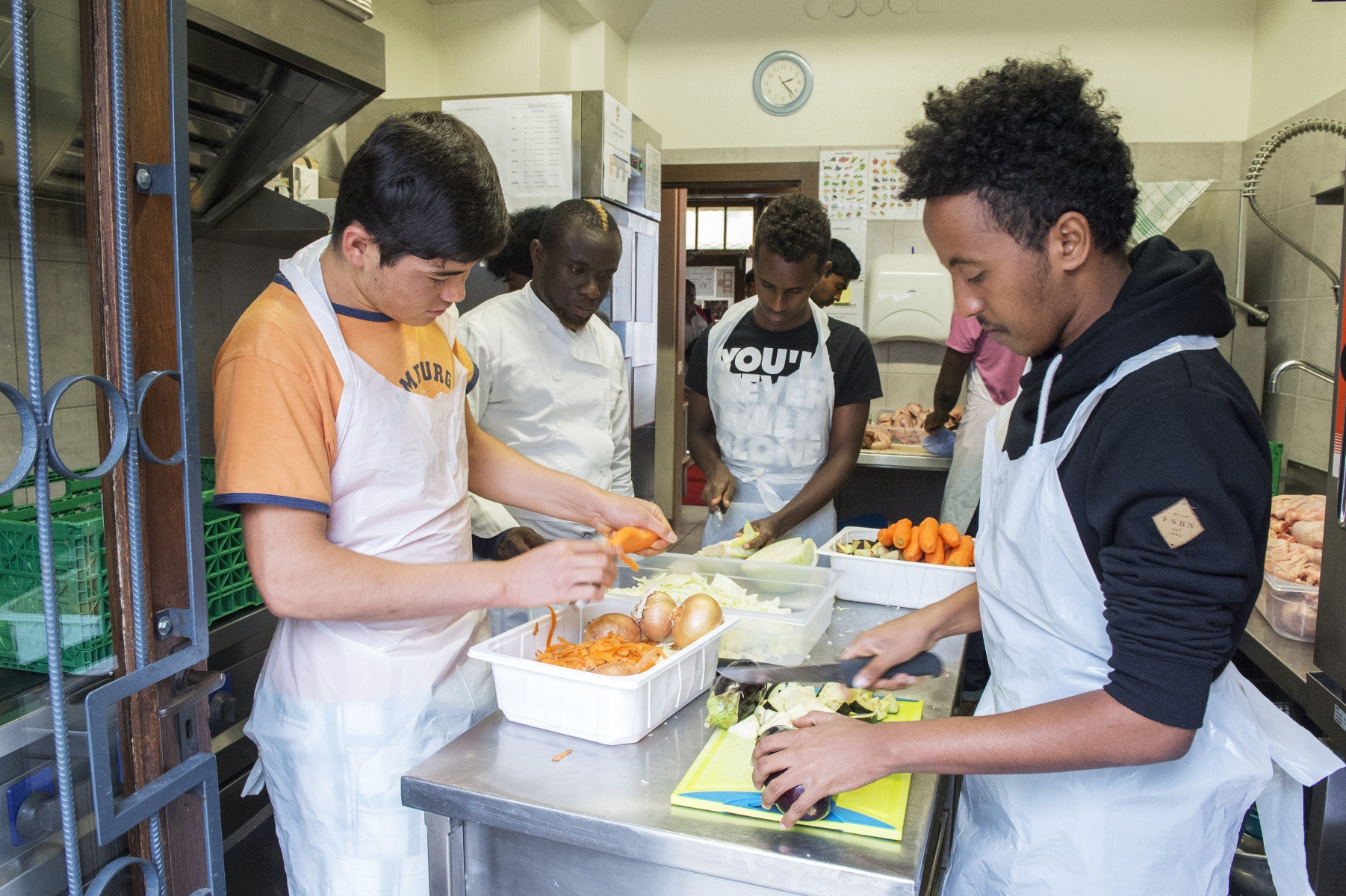 Dans la cuisine du Rados, des jeunes requérants d'asile préparent le repas sur les conseils de Gaby Yao, encadrant éducatif.