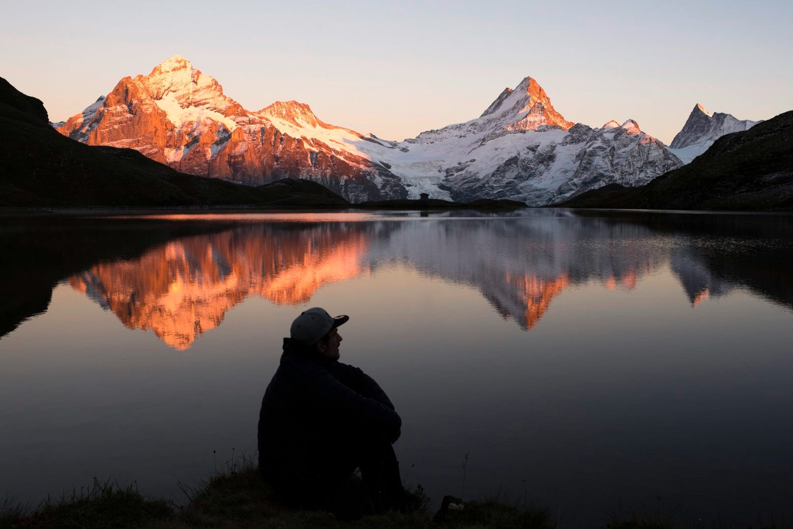 A man looks at the mountains Wetterhorn, Lauteraarhorn, Schreckhorn and Finsteraarhorn that are reflecting during the sunset in the Bachalpsee lake (2265m) close to the First, above Grindelwald in the Bernese Oberland, Switzerland, on Monday, October 3, 2016. (KEYSTONE/Anthony Anex) SWITZERLAND SUNSET ALPS GRINDELWALD