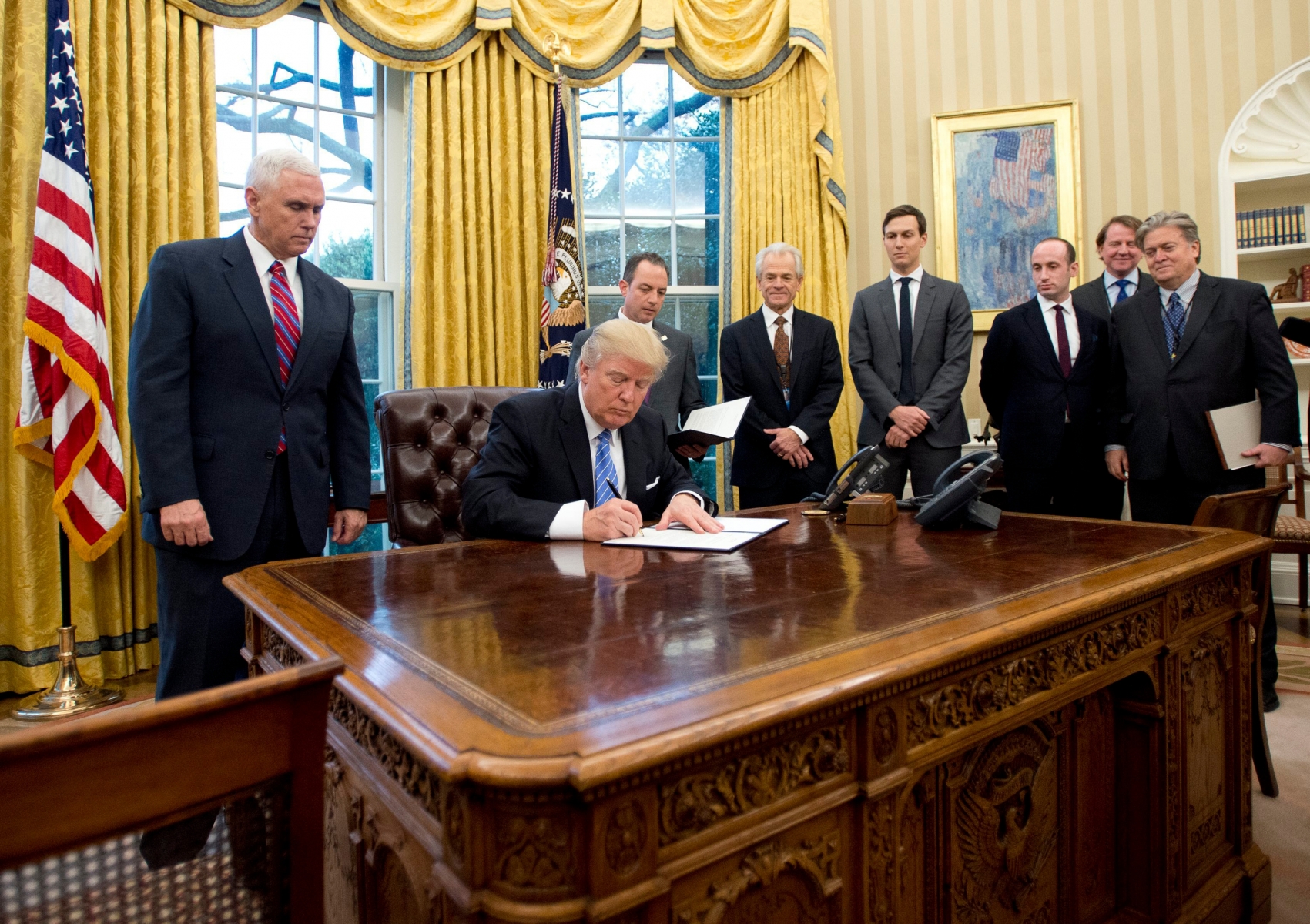 epa05744781 US President Donald J. Trump signs the first of three Executive Orders in the Oval Office of the White House in Washington, DC, USA, 23 January 2017. They concerned the withdrawal of the United States from the Trans-Pacific Partnership (TPP), a US Government hiring freeze for all departments but the military, and "Mexico City" which bans federal funding of abortions overseas. Standing behind the President, from left to right: US Vice President Mike Pence; White House Chief of Staff Reince Preibus; Peter Navarro, Director of the National Trade Council; Jared Kushner, Senior Advisor to the President; Steven Miller, Senior Advisor to the President; unknown; and Steve Bannon, White House Chief Strategist.  EPA/Ron Sachs / POOL USA TRUMP
