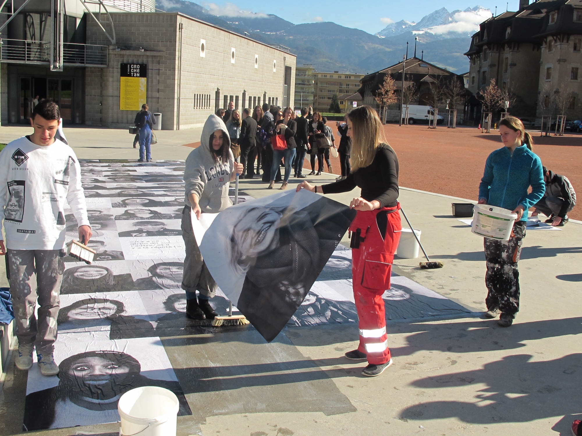 Des jeunes du SEMO de Monthey en train de coller des photos géantes devant le Théâtre du Crochetan.