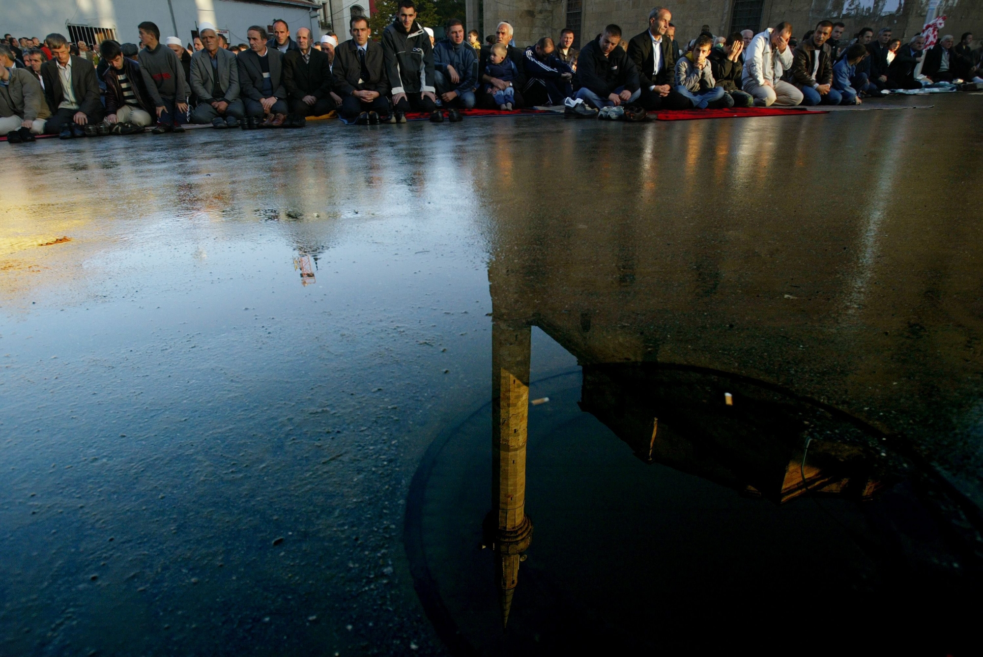 Reflection of the Grand Mosque is seen in a pudle of water as Kosovo muslims are lined up in the streets of capital Pristina on Monday, Oct. 23, 2006, after prayers marking the first day of Eid al-Fitr celebrations, the end of the holy month of Ramadan.. (AP Photo / Visar Kryeziu) KOSOVO RAMADAN