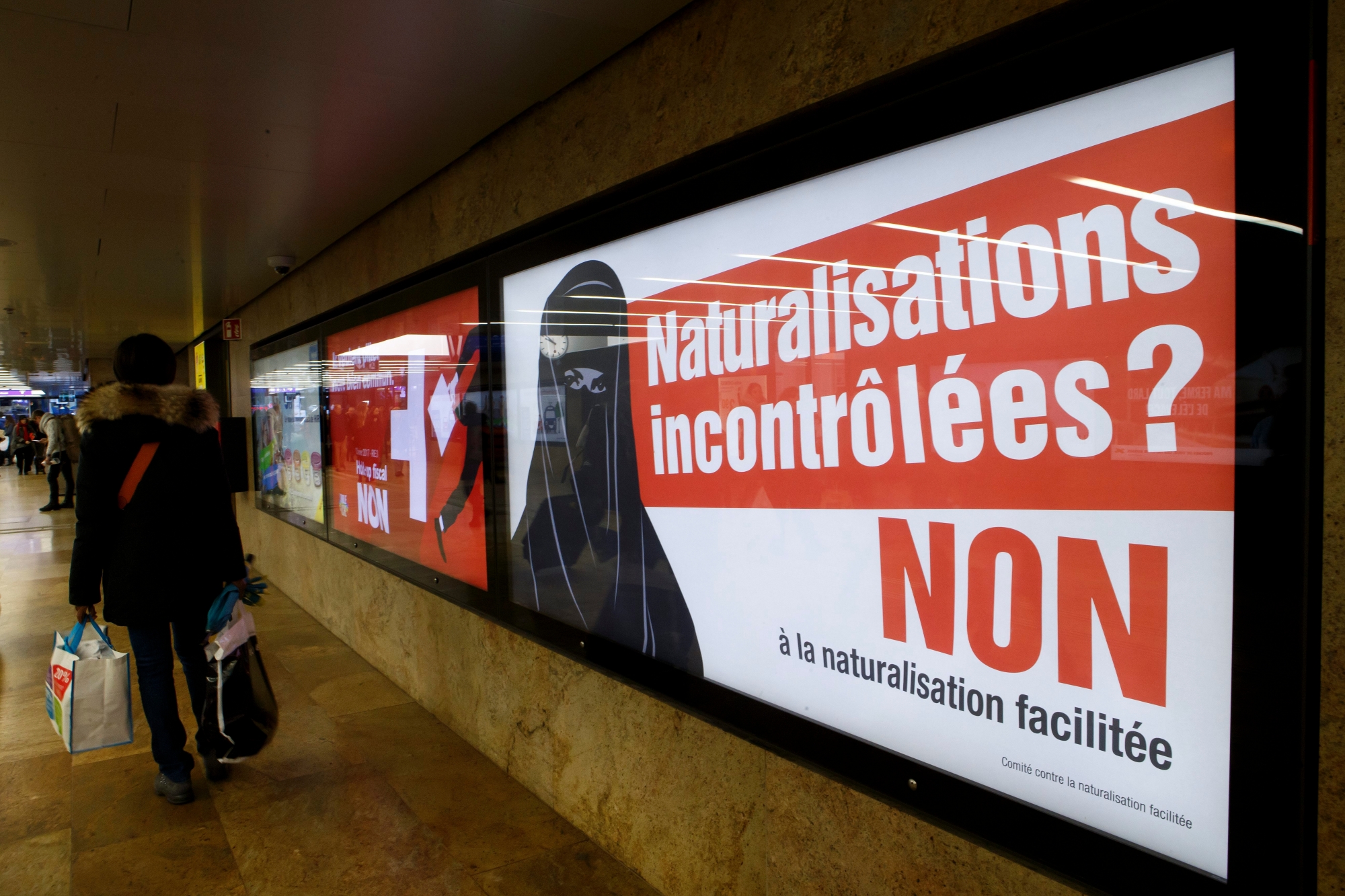 A woman passes in front of a poster of the right-wing Swiss People's Party (SVP/UDC) which shows a woman wearing a burqa with the slogan "Uncontrolled naturalization? No to the naturalization facilitated", in Geneva, Switzerland, Saturday, February 4, 2017. Swiss citizens will vote on February 12 on the Federal Decree on the Simplified Naturalisation of Third-Generation Immigrants. (KEYSTONE/Salvatore Di Nolfi) SWITZERLAND FEDERAL VOTE SWISS NATURALIZATION