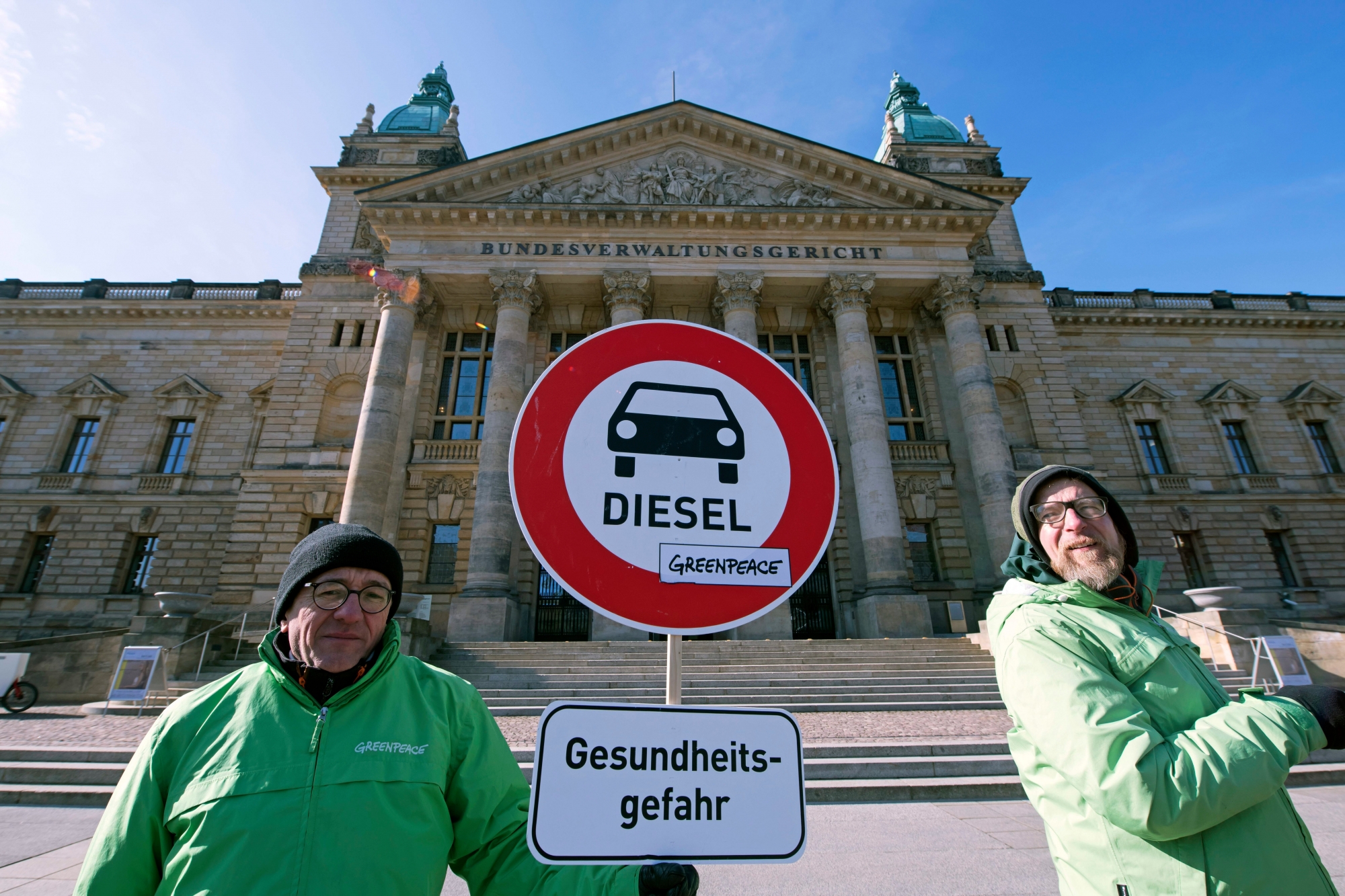 Environment activists stand in front of the Federal Administrative Court prior to a trial in Leipzig, Germany, Tuesday, Feb. 27, 2018. The German court ruled Tuesday that cities can impose driving bans on diesel cars to combat air pollution, a decision that could affect millions of drivers and the country's powerful auto industry. Sign below reads: Health Risk.  (AP Photo/Jens Meyer) Germany Diesel Ban