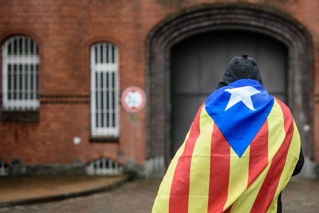 epa06640130 Catalan sympathizer Eduardo Alonso has a Catalonian Independence flag wrapped around his shoulders as he waits in front of the 'Justizvollzugsanstalt (JVA) Neumuenster' prison, where the detained former Catalan leader Carles Puigdemont is detained in Neumuenster, Germany, 01 April 2018. German police on 25 March 2018 detained former Catalan leader Puigdemont after he crossed into Germany from Denmark. Puigdemont is sought by Spain who issued an European arrest warrant against the former leader who is living in exile in Belgium.  EPA/CLEMENS BILAN