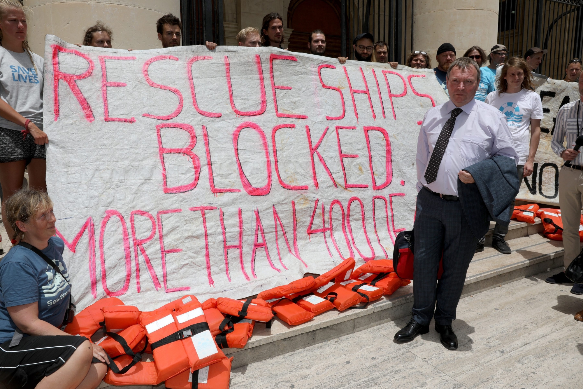 epa06857606 Claus-Peter Reisch (C), the captain of the Lifeline NGO vessel rescue ship with 234 migrants on board which finally berthed in Malta on 27 June 2018, is seen posing near a banner at the Malta Law Courts after being arraigned in court in Valletta, Malta, on 02 July 2018.  EPA/DOMENIC AQUILINA MALTA MIGRATION LIFELINE