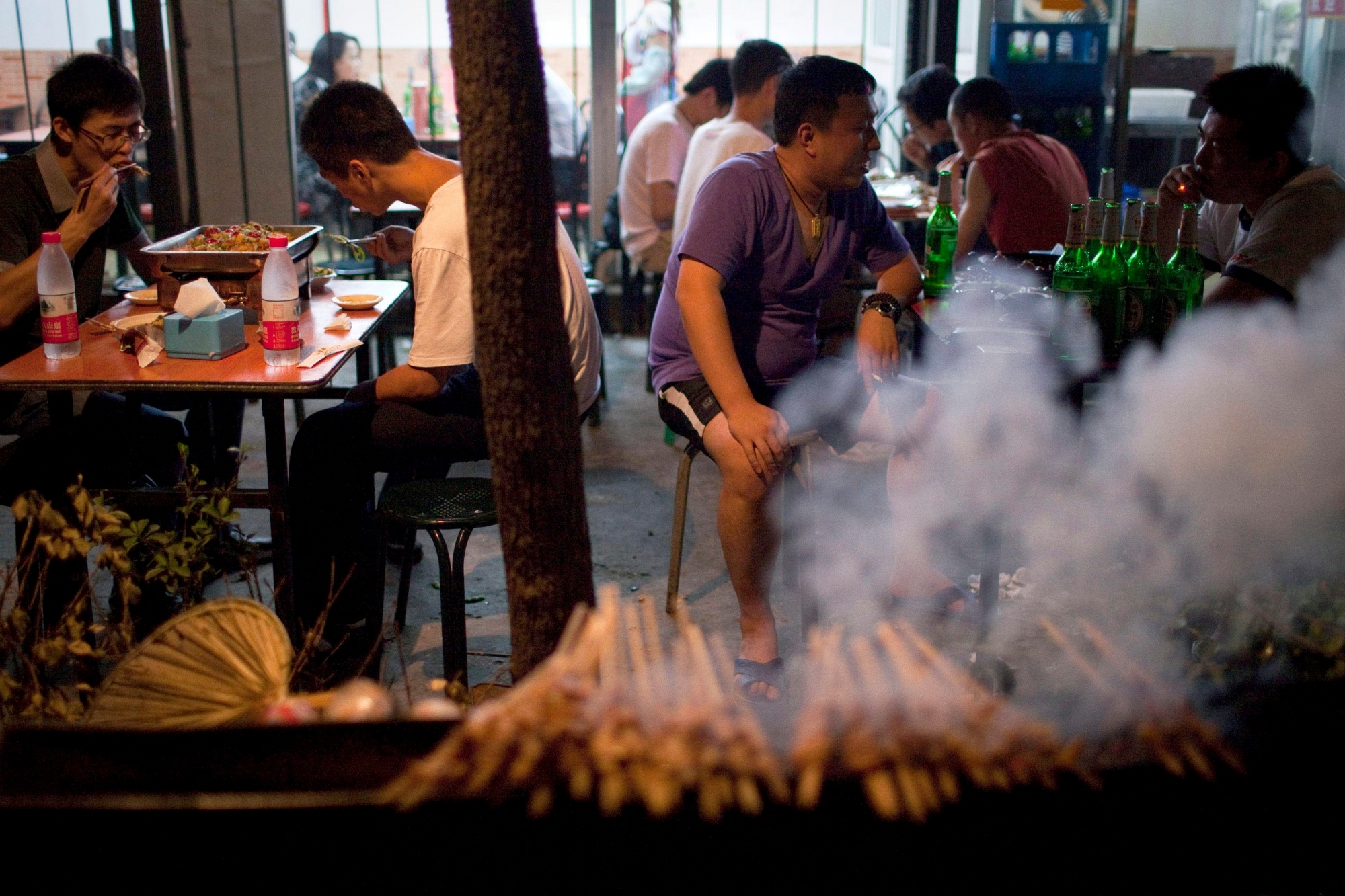 ADVANCE FOR RELEASE THURSDAY, SEPTEMBER 15, 2011, AT 12:01 A.M. EDT - In this Aug. 22, 2011 photo, people smoke cigarettes and drink beers while eating near a barbecue grill at an outdoor food stall in Beijing, China. Heart disease, cancer, and respiratory disease have replaced hepatitis, diarrhea and malaria as desk work replaces farming, cars replace bicycles, and smoking remains stubbornly popular. (AP Photo/Alexander F. Yuan) China Chronic Disease