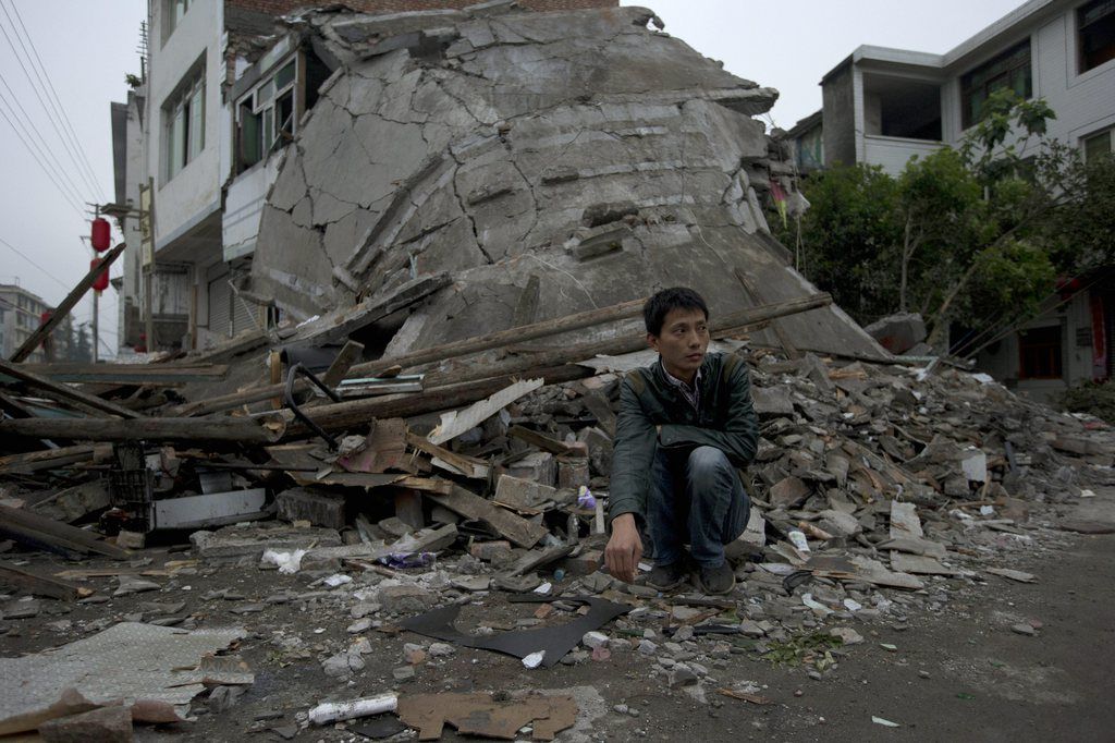 A man squats near the collapsed remains of a building destroyed by Saturday's earthquake in Lushan county in southwestern China's Sichuan province, Monday, April 22, 2013. Saturday's earthquake in Sichuan province killed at least 186 people, injured more than 11,000 and left nearly two dozen missing, mostly in the rural communities around Ya'an city, along the same seismic fault where a devastating quake to the north killed more than 90,000 people in Sichuan and neighboring areas five years ago in one of China's worst natural disasters.(AP Photo/Ng Han Guan)