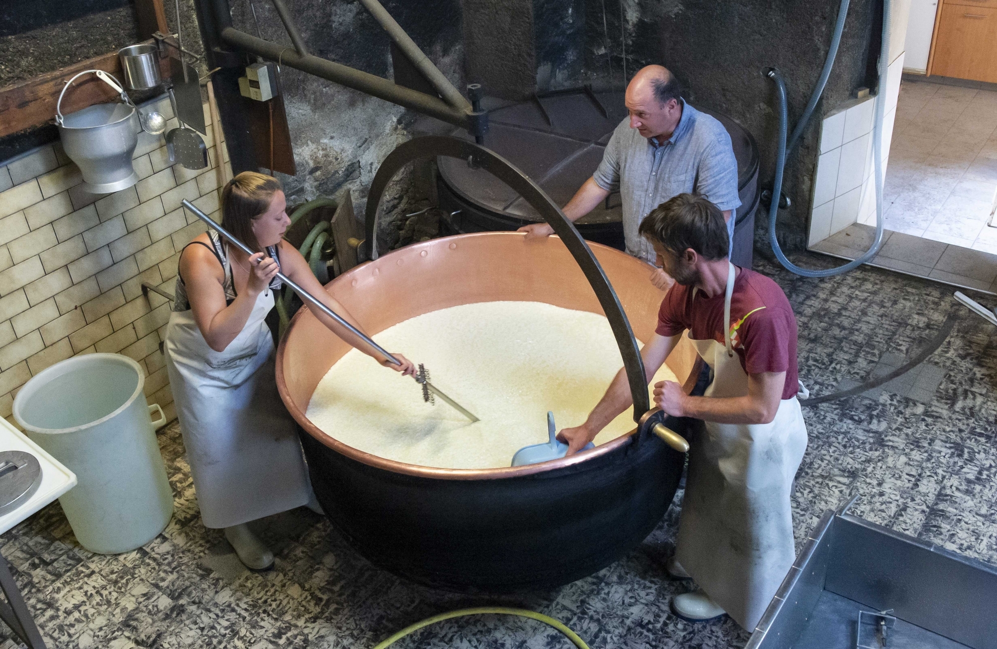 Martina et Frédéric s'apprêtent à fabriquer leur millième pièce de fromage à raclette au feu de bois sur l’alpage du Cœur sous le regard d'Eric Masseraz, le conseiller en économie laitière au canton du Valais.
